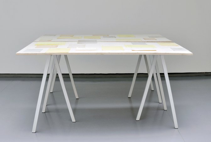Overview of installation with works on paper arranged on two tables. Photography.